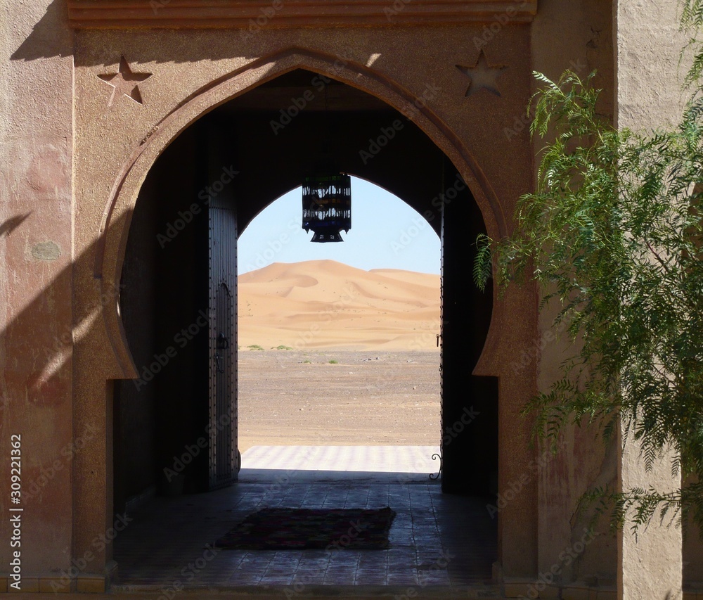 Arched door with tiled entryway,  view of sunlit Sahara sand dunes, hanging lantern -Nomad Palace, Morocco, Inshallah