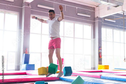 Fitness  fun  leisure and sport activity concept - Handsome happy man jumping on a trampoline indoors
