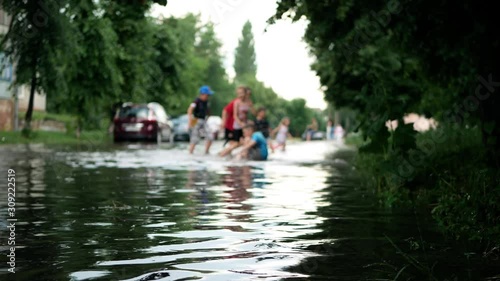 Wet people children kids play in dirty water on the flooded city street after heavy rain. Disaster flood deluge and water flow after rainfall. Natural weather disaster-cataclysm 