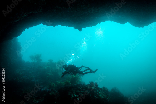 A couple of scuba divers exploring the bottom of an underwater arch.