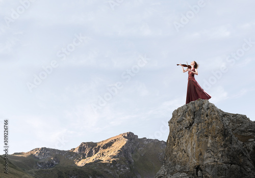 Woman violinist in red dress playing melody against cloudy sky