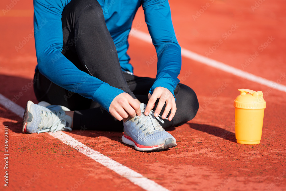Close up view, of an athlete tying his shoe laces. Man tightening his shoe laces sitting on the ground on a running track .