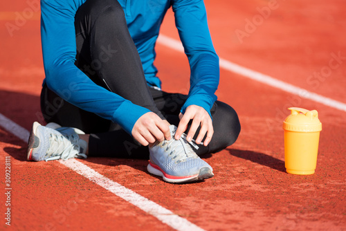 Close up view  of an athlete tying his shoe laces. Man tightening his shoe laces sitting on the ground on a running track .