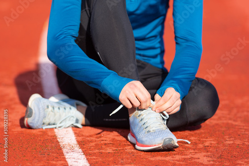 Close up view  of an athlete tying his shoe laces. Man tightening his shoe laces sitting on the ground on a running track .