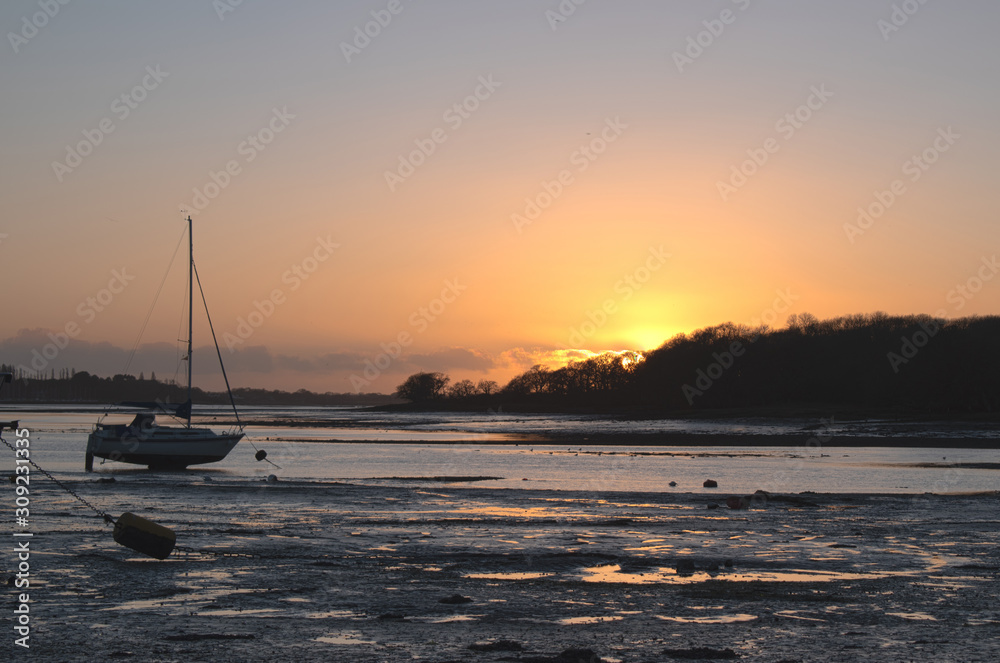 Sunset at Dell Quay sailing club near Chichester. Sun just over the horizon setting in a blaze of colours and reflecting of the water and sand at low tide.