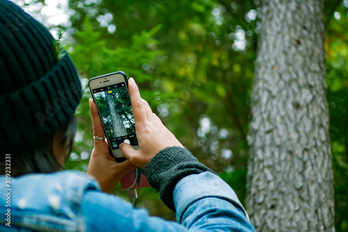 Close up back view of a person taking picture of forest using a smartphone. Blurred forest as background 