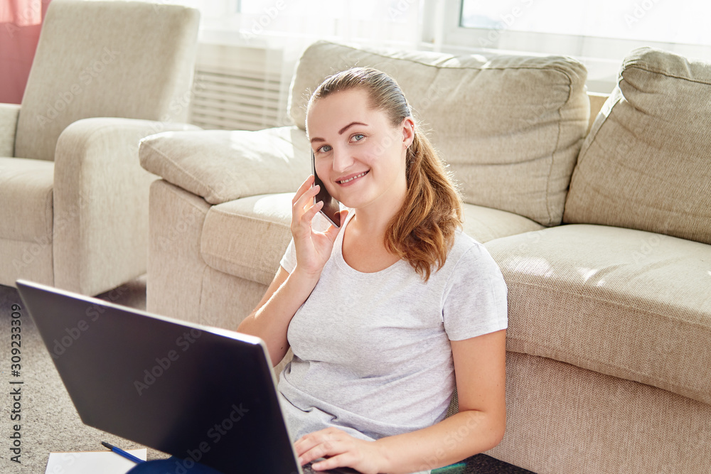 Portrait of happy smiling young woman lying on floor, using laptop and talking on phone at home, copy space