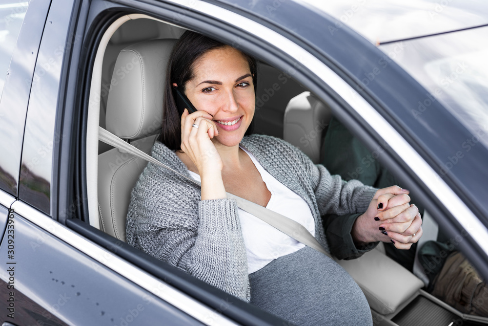 Beautiful pregnant woman is talking on the phone in the car