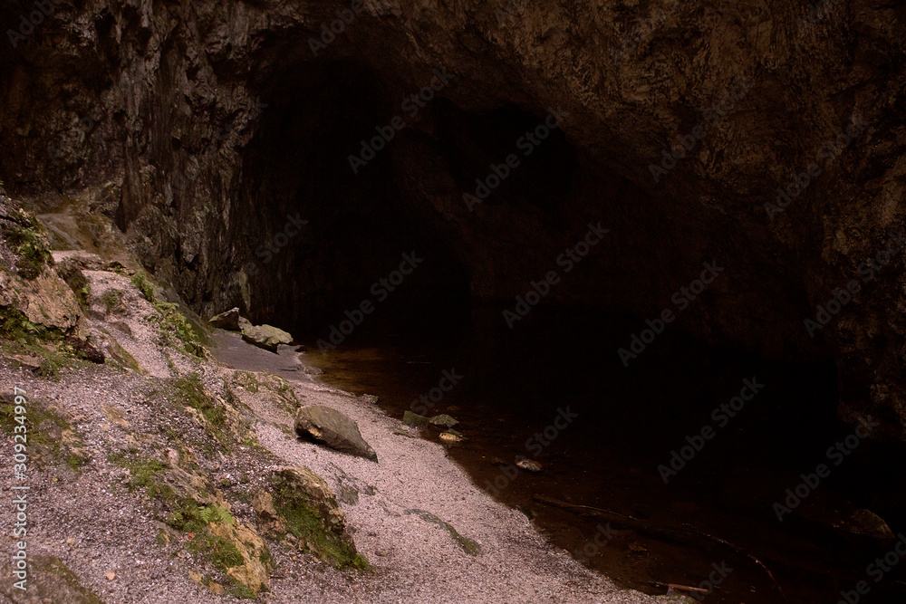 Dark interior of the cave. Abstract natural background with dark zone. Shore of an underground lake. Deep shadow. Mysterious background. Copy space.