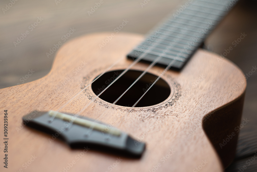 Fototapeta premium Defocused ukulele body, soundhole, bridge and neck on brown wooden background.