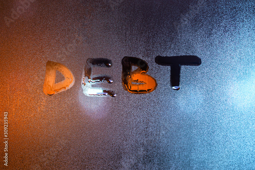 the word debt written on night wet window glass close-up with blurred background photo