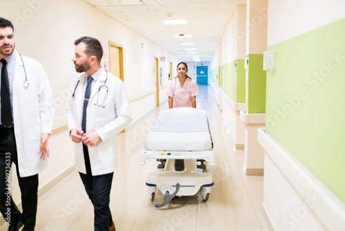 Nurse Walking With Stretcher While Doctors Discussing At Hospital