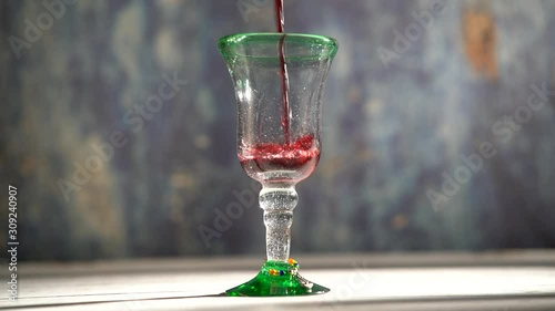 Seamless, looping clip of red wine pouring into a rustic glass with blue background. photo