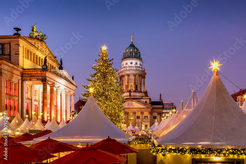 Der Weihnachtsmarkt am Gendarmenmarkt in Berlin am Abend mit den beleuchteten, historischen Gebäuden und festlich geschmücktem Tannenbaum