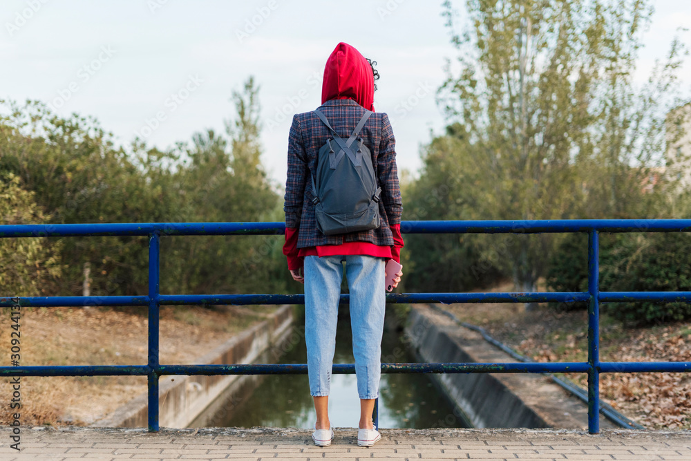 Back view of young woman with backpack and mobile phone standing on a bridge Back view of young woman with backpack and mobile phone standing on a bridge