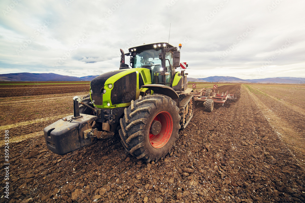 Modern tractor working on the farm, a modern agricultural transport, cultivation of fertile land, tractor on cloudy sky background, agricultural machine. Tractor in full speed Modern tractor working on the farm, a modern agricultural transport, cultivation of fertile land, tractor on cloudy sky background, agricultural machine. Tractor in full speed