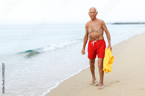 Glad man in beachwear resting near ocean