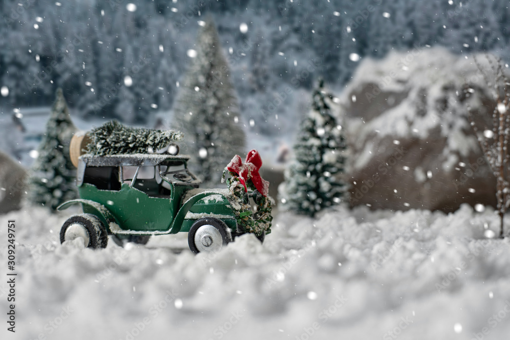 Miniature classic car carrying a christmas tree on snowy winter landscape
