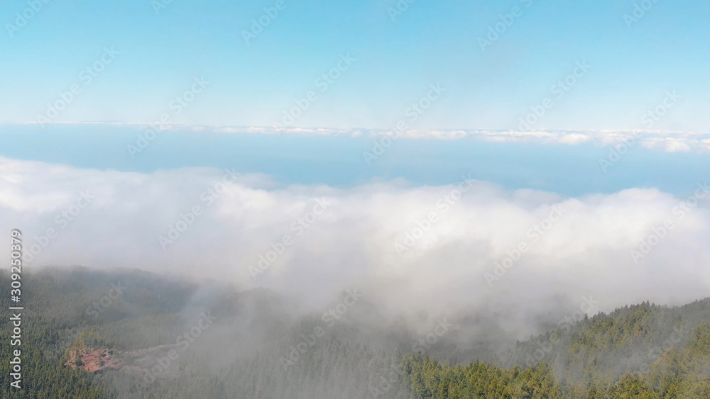 Drone flies through the clouds above a thick green forest. Lots of clouds over the valley. Tenerife Island, Spain