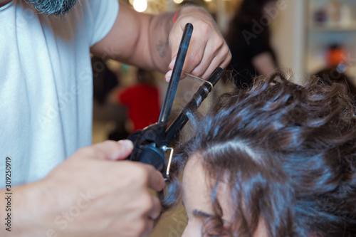 hairdresser straightening hair over . blonde doing the Curling irons in the beauty salon . Professional hairdresser . Close up of stylist's hand using curling iron working for woman client hair .