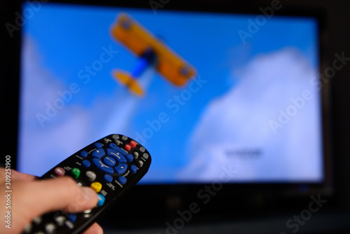 Canvas Print Man pointing a universal remote control towards a television screen to change th