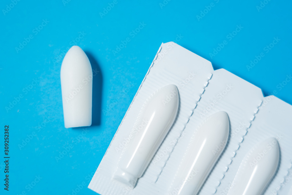 Obraz premium White suppositories for anal or vaginal use on blue background. Medical candles for treatment of Candida, thrush, hemorrhoids, inflammation and fever. Effective drug for timely treatment of diseases