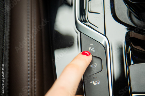 the finger of a female hand points to the parking assistant button, the equipment of a modern car. close-up, soft focus, blur background