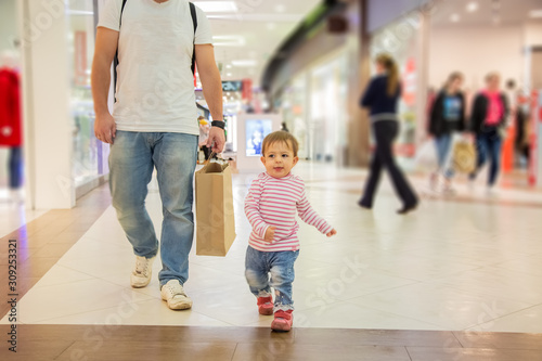Black friday sale concept, shopping with children. little cute girl is walking along the mall with dad with a craft paper bag for shopping. close-up, soft focus, blur background