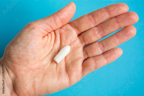 White suppository for anal or vaginal use in patient's hand on blue background. Medical candles for the treatment of Candida, thrush, hemorrhoids, inflammation and fever. Effective drug. Copy space