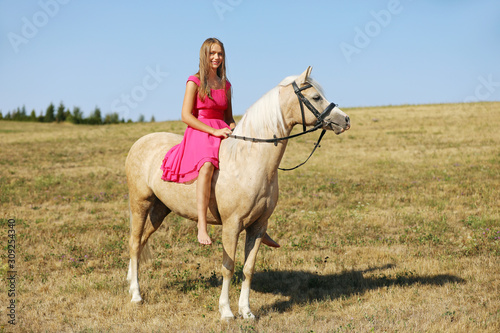Teen girl on palomino ponny in pink dress without saddle in sunny afternoon