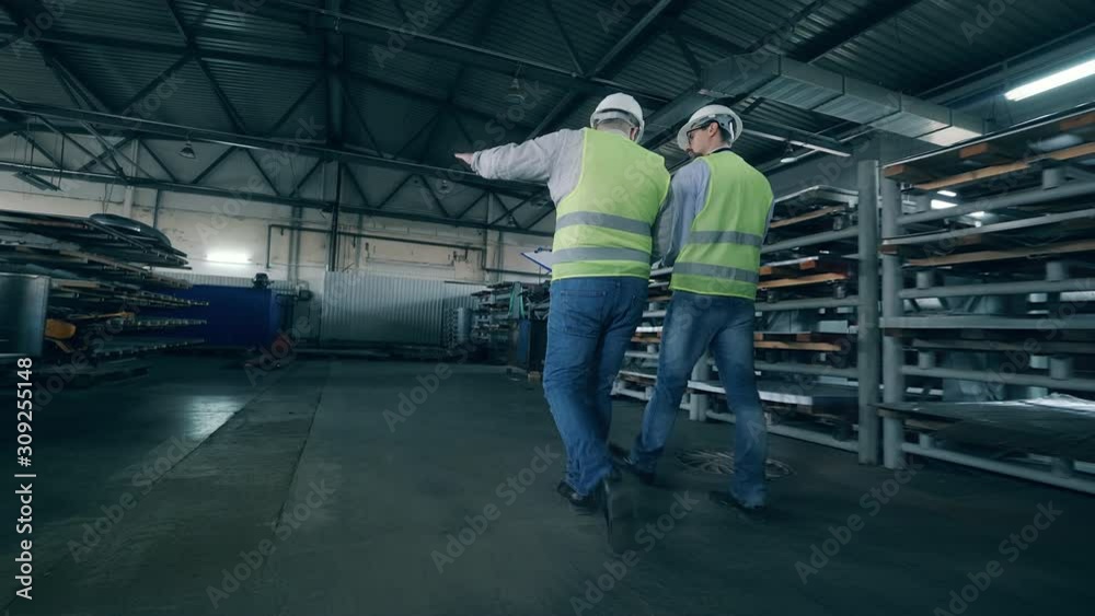 Two male workers are walking along factory premises Two male workers are walking along factory premises