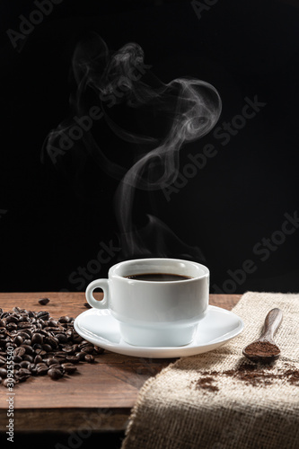 Warm coffe smoke, with .coffee beans. wooden spoon with coffe on wooden base, on dark background.