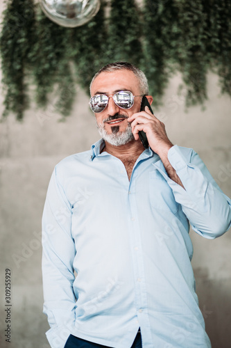 Middle age man with beard and with sunglasses talking on the phone.