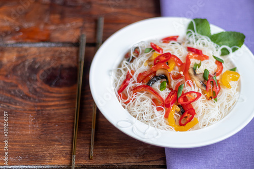 Oriental rice noodles Udon with sweet pepper, mushrooms. On a wooden background.