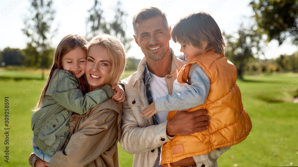Daughter and son. Portrait of happy and beautiful family with children looking at camera with smile while standing in the park on a sunny day Daughter and son. Portrait of happy and beautiful family with children looking at camera with smile while standing in the park on a sunny day