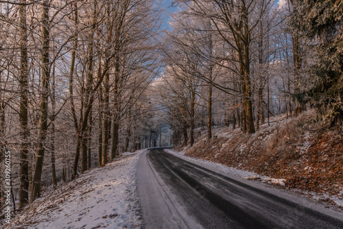 Winter morning with snowy road in color forest in Krusne mountains