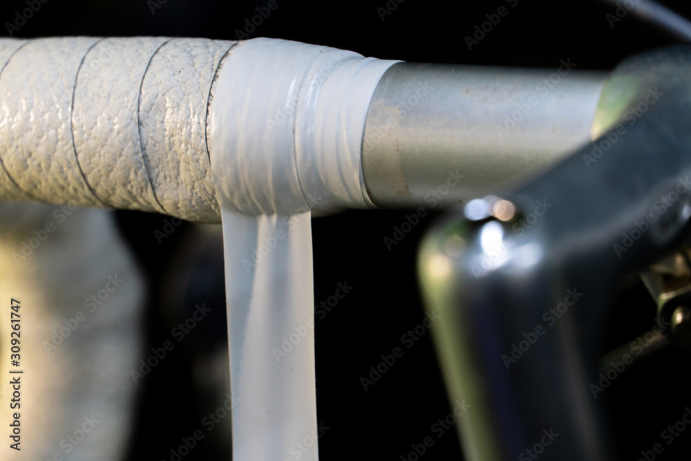 Road bike handlebars and dual control lever on a black background. Install handlebar tape white. Bicycle repair in a modern workshop. White insulating tape close-up. Road bike handlebars and dual control lever on a black background. Install handlebar tape white. Bicycle repair in a modern workshop. White insulating tape close-up.