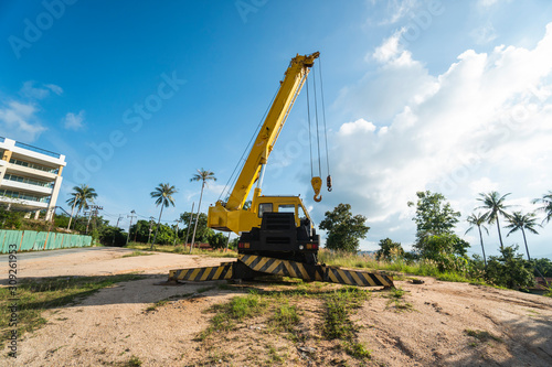 Yellow automobile crane with risen telescopic boom outdoors. Mobile construction crane on a constructin site. Crane machine stand by waiting for work under the construction building. Heavy industry.