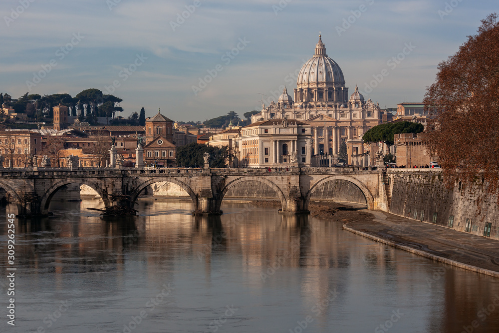 Sant'Angelo Bridge through the Tiber River and the dome of St. Peter's Basilica in Rome in sunny winter morning, Italy