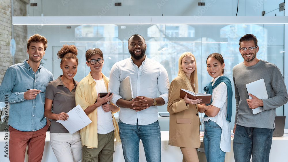 © Svitlana - Dream work. Portrait of young and successful co-workers in casual wear smiling at camera while standing in working space