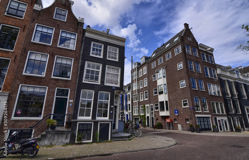 Amsterdam, Holland, August 2019. The typical houses of the historic center: made of brick and with white window frames. People walk in the street. Amsterdam, Holland, August 2019. The typical houses of the historic center: made of brick and with white window frames. People walk in the street.