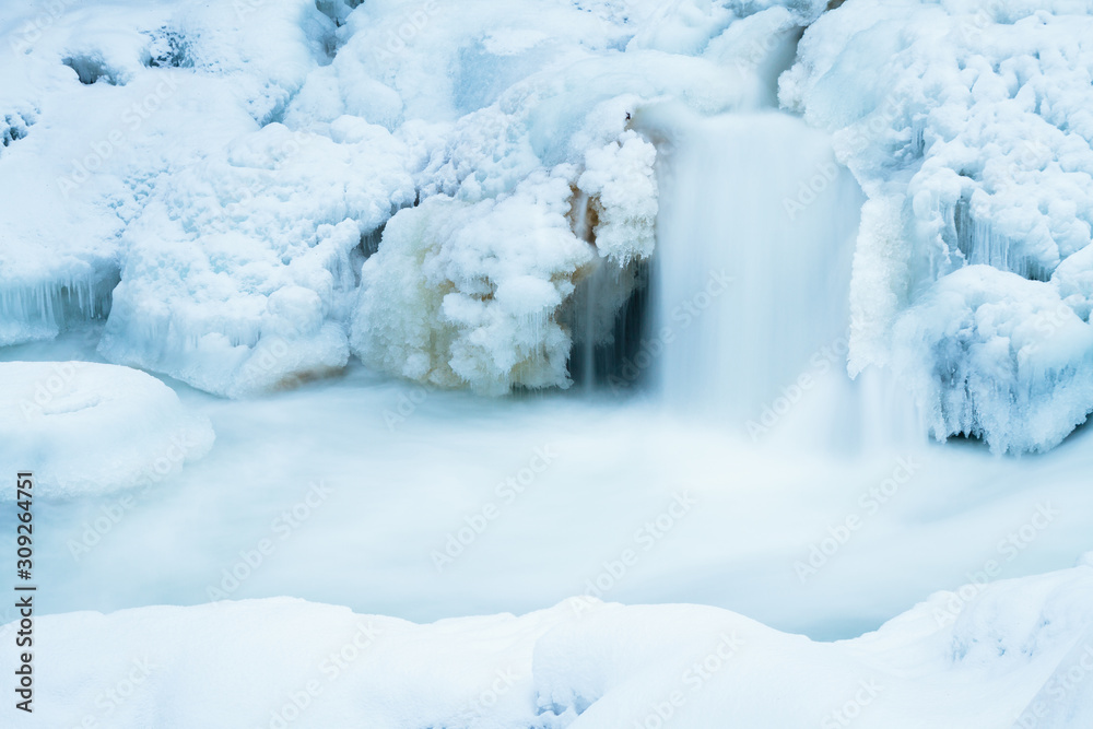 Canadian waterfall flowing in winter over ice. snow bank at the front. 