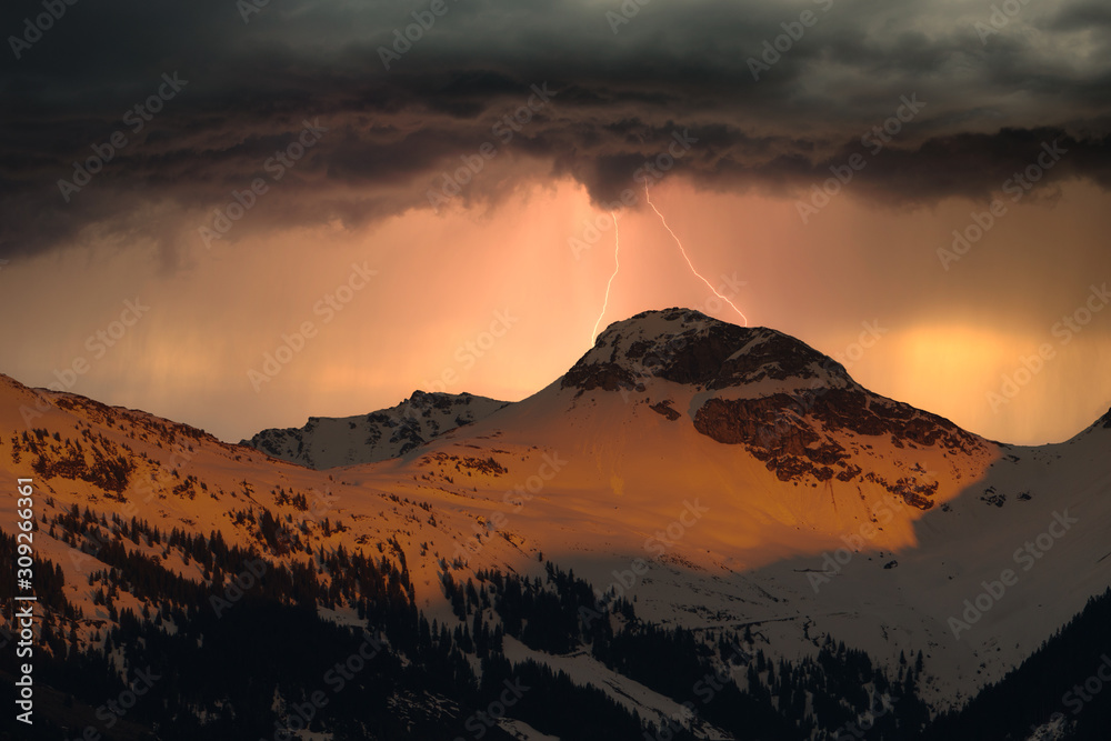 Fototapeta premium schneebedeckte Berge mit Gewitterwolken und Blitz
