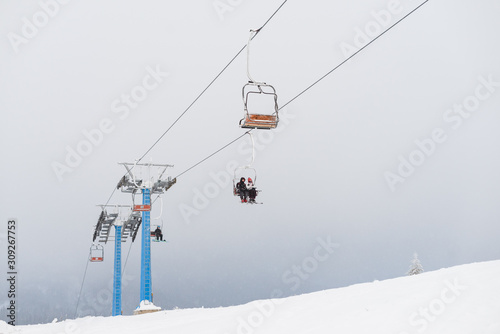 Chairlift moving in foggy and snowy day. Snow covered trees on the hills surrounding.