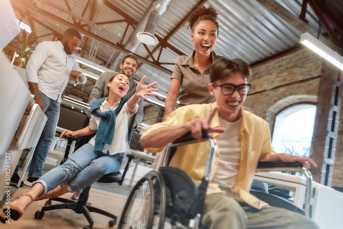 Being disabled does not mean you can't be happy. Young positive asian man in wheelchair having fun with his colleagues at modern office