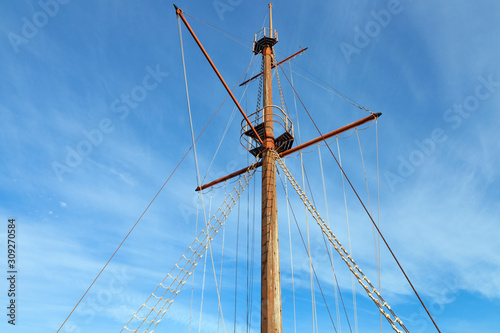 Wooden top of the old sailing ship mast, yards and rigging against blue sky .