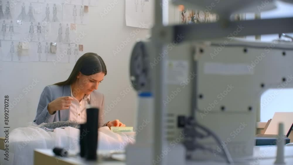Sewing workshop girl sitting at the table in hand sew beads and jewelry. Sew dresses and decorate evening dresses with crystals Sewing workshop girl sitting at the table in hand sew beads and jewelry. Sew dresses and decorate evening dresses with crystals