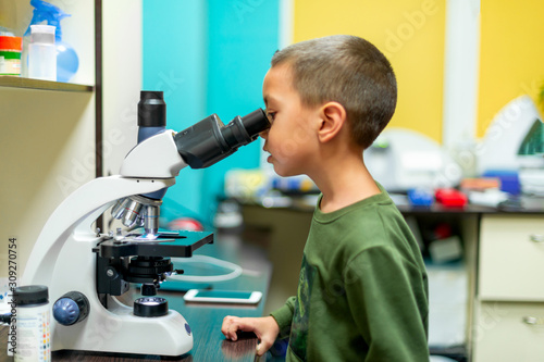 The little boy looks through a microscope in a laboratory with curiosity.  Children came on an excursion to the clinic.
