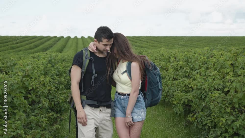 Lovely couple walks with rucksacks and watching on currant plantation