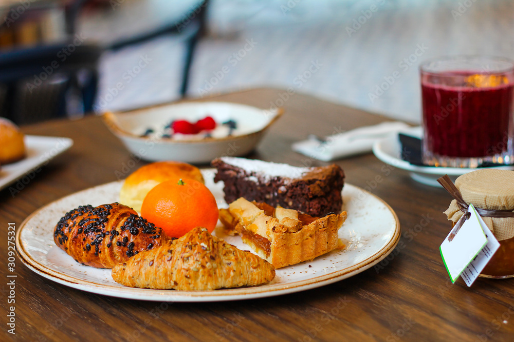 detail of breakfast table with chocolate cakes, jam, red orange juice, mandarin, croissants, butter, yogurt with raspberries and blueberries